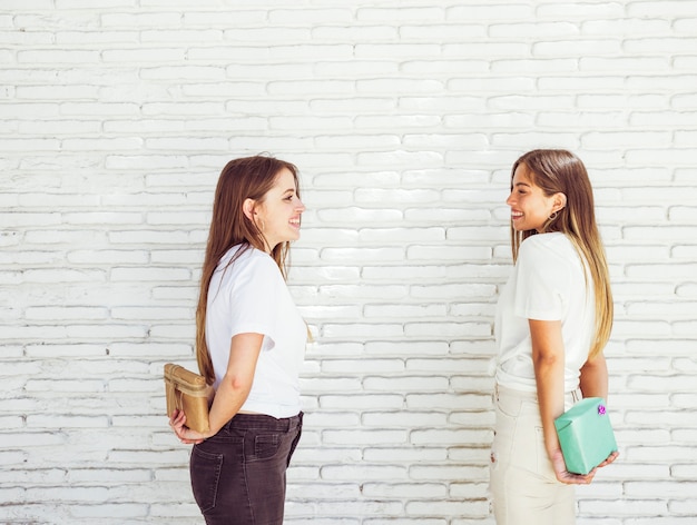 Free photo two happy female friends hiding birthday gift from each other