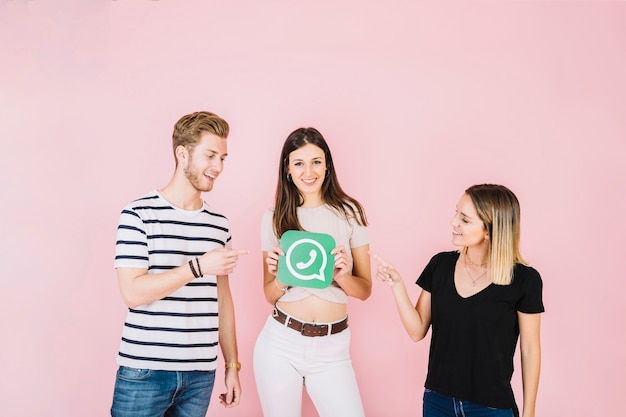 Two happy friends pointing at woman holding whatsapp icon