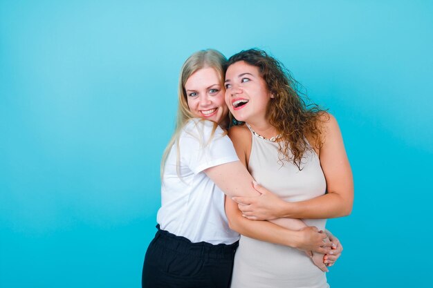 Two happy girls are laughing by hugging each other on blue background