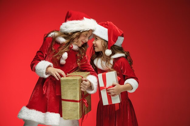 Two happy girls in santa claus hats with gift boxes at red studio