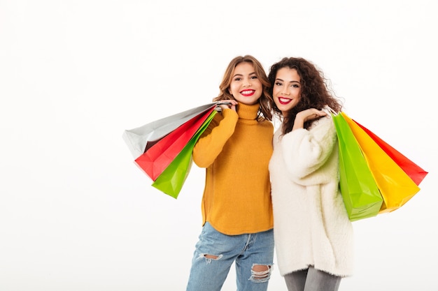 Due ragazze felici in maglioni con pacchetti guardando la telecamera sul muro bianco