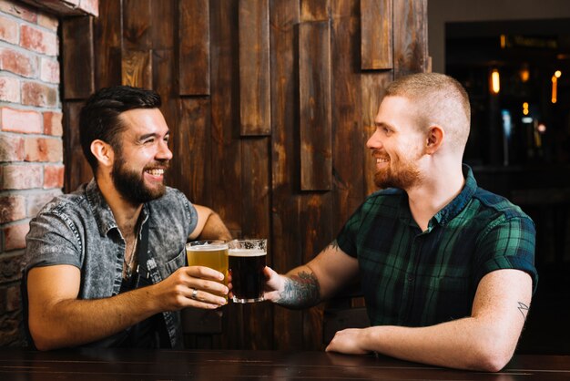 Two happy male friends toasting alcoholic glasses in bar