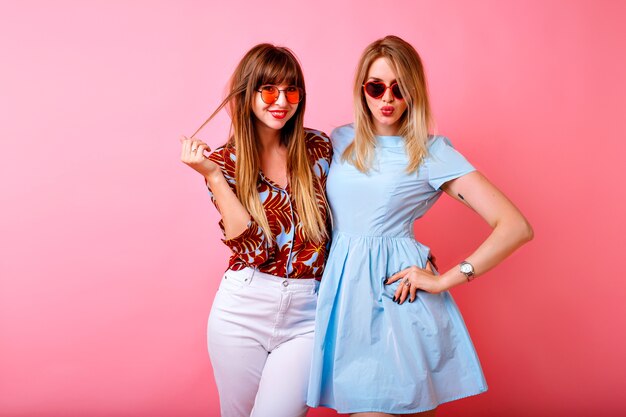 Two happy pretty sisters best friends hipster women having fun together at pink studio background