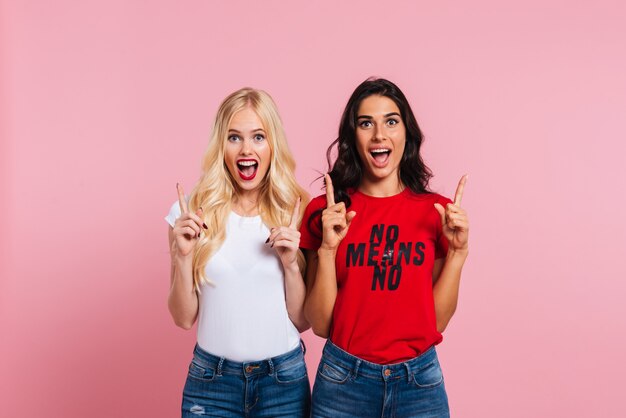 Two happy screaming women showing size of something and looking at the camera over pink background