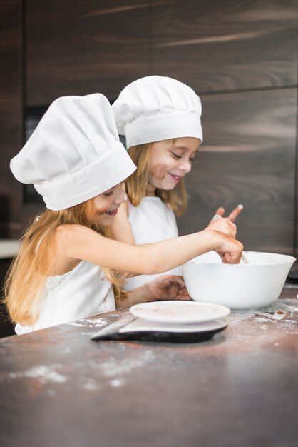 Two happy siblings preparing food in bowl on dirty kitchen counter