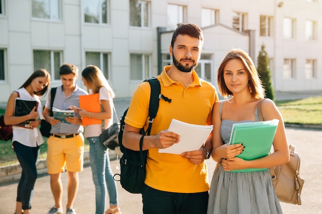 Two happy students with backpacks and books in their hands smiling at camera 