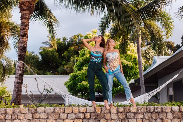 Две счастливые подруги в солнцезащитных очках на отдыхе в тропической стране