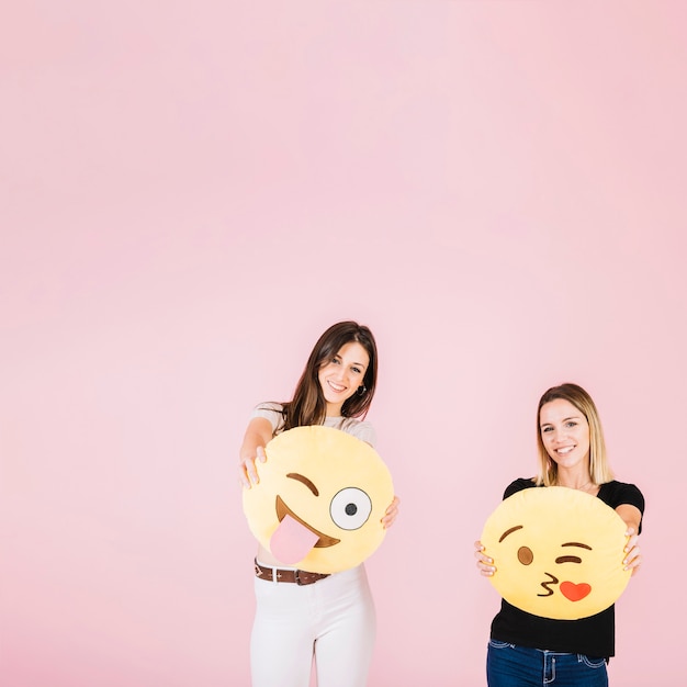 Две счастливая женщина с различными значками emoji на розовом фоне