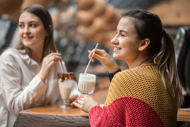 Две счастливые женщины сидят в кафе, пьют молочные коктейли,