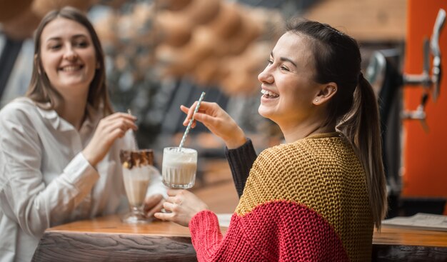 2人の幸せな女性がカフェに座って、ミルクセーキを飲んでいます。