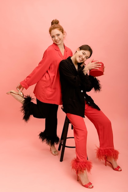 Две счастливые молодые кавказские женщины брюнетка и рыжая смотрят в камеру на розовом фоне Концепция дружбы