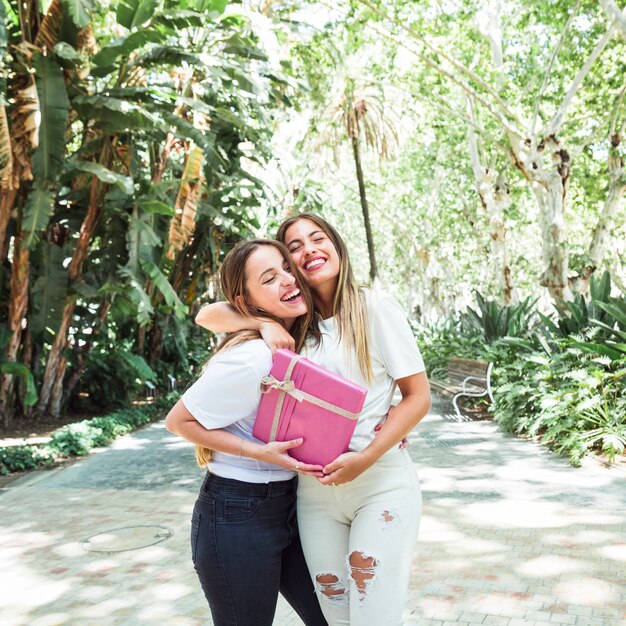 Two happy young women with pink gift box standing in park