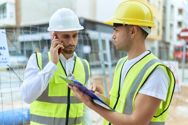 Free photo two hispanic men architects writing on document talking on smartphone at street