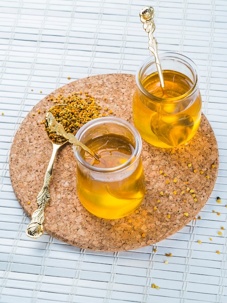 Two honey pots with bee pollen on circular cork coaster over placemat