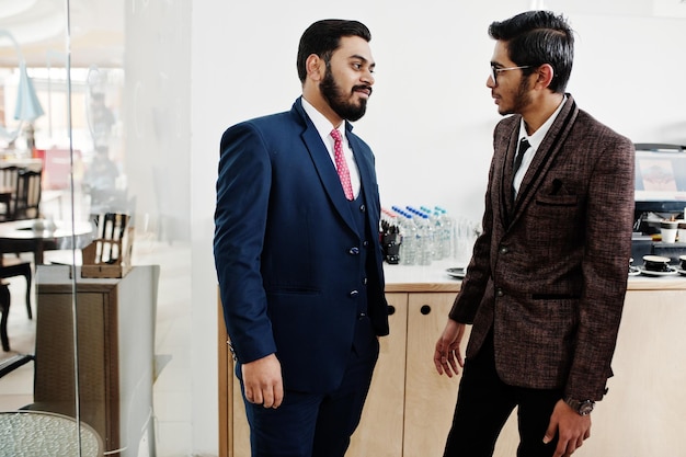 Два индийских бизнесмена в костюмах стоят в кафе и обсуждают друг друга