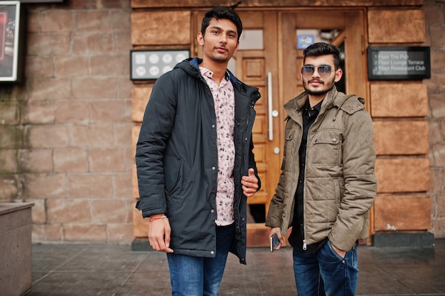 Два индийских парня в куртках позируют на улице у двери паба