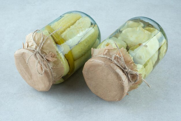 Two jars of pickled vegetables on blue surface.