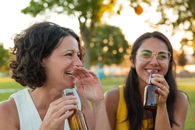 Two joyful female friends drinking beer and having fun