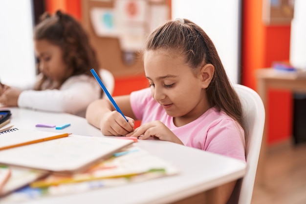 Two kids preschool students sitting on table drawing on paper at classroom