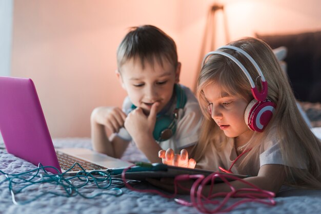 Two kids with laptop and tablet on bed