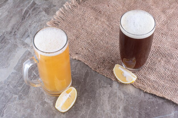 Два вида пива на мраморной поверхности с лимонами. Фото высокого качества