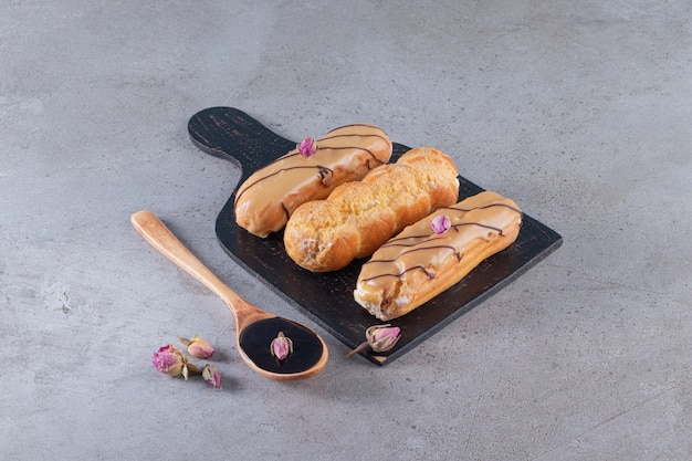 Two kinds of chocolate eclairs with spoon of chocolate on stone surface.