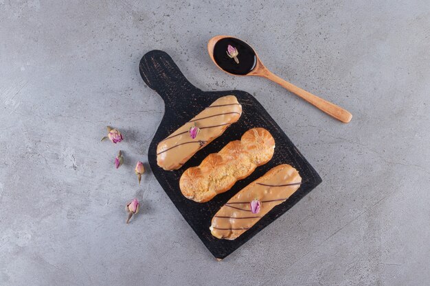 Two kinds of chocolate eclairs with spoon of chocolate on stone table. 