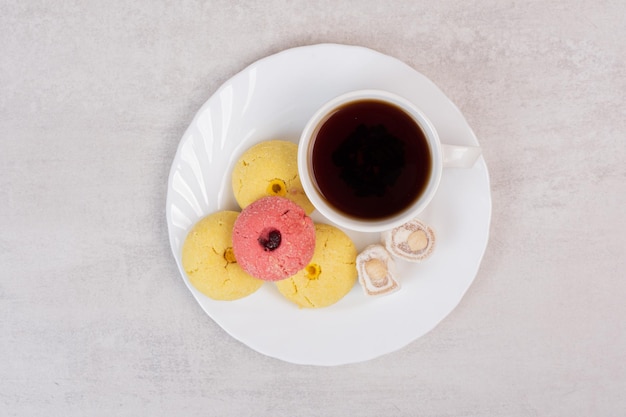 Two kinds of cookies, delights and cup of tea on white plate.