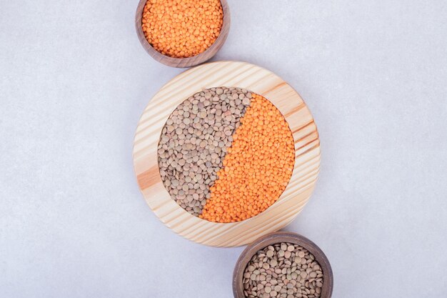 Two kinds of raw beans and lentils in wooden plate and bowls.