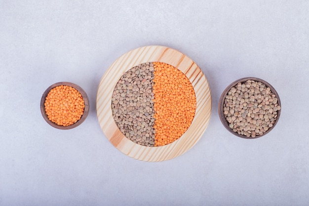 Free photo two kinds of raw beans and lentils in wooden plate and bowls.