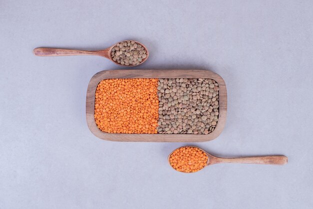 Two kinds of raw beans and lentils in wooden plate with spoons.