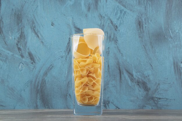 Two kinds of raw pasta in glass on blue surface