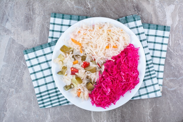 Two kinds of sauerkraut and pickles on white plate with tablecloth.