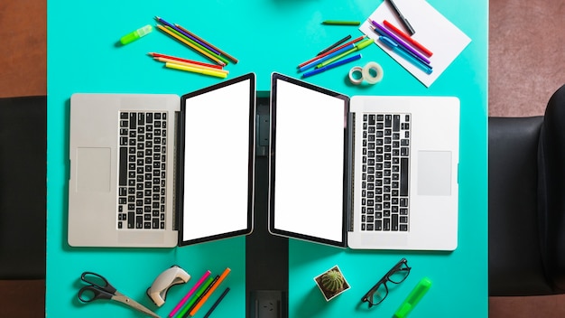 Two laptop with blank screen display on office desk with stationeries and chair near by