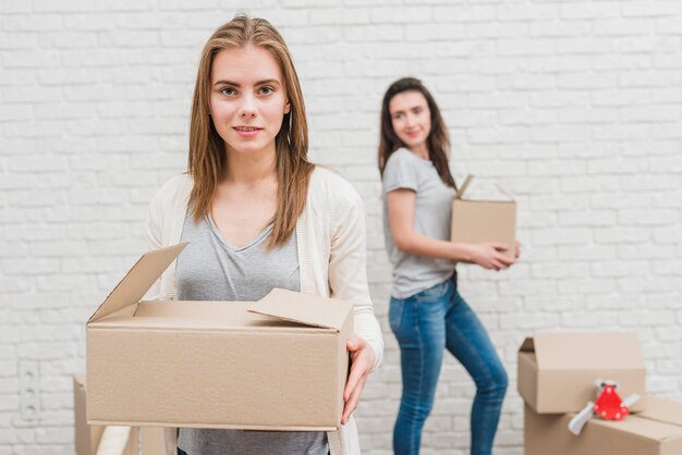 Two lesbian women holding cardboard boxes in hand standing near the white brick wall