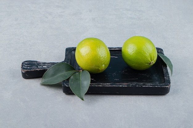 Foto gratuita due frutti di lime con foglie sul tagliere.