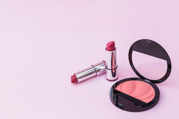 Two lipsticks and pink blusher on pink background