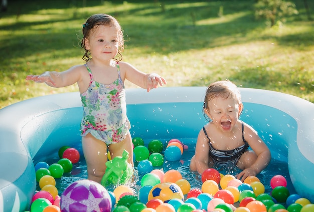 The two little baby girls playing with toys in inflatable pool in the summer sunny day