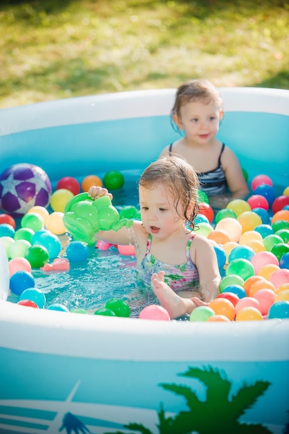 Free photo the two little baby girls playing with toys in inflatable pool in the summer sunny day