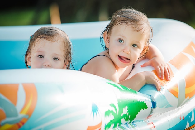 夏の晴れた日に膨脹可能なプールでおもちゃで遊ぶ2人の小さな女の赤ちゃん