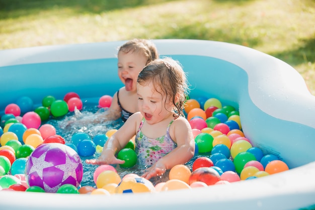 夏の晴れた日に膨脹可能なプールでおもちゃで遊ぶ2人の小さな女の赤ちゃん
