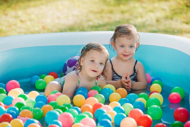 Две маленькие девочки играют с игрушками в надувном бассейне в солнечный летний день