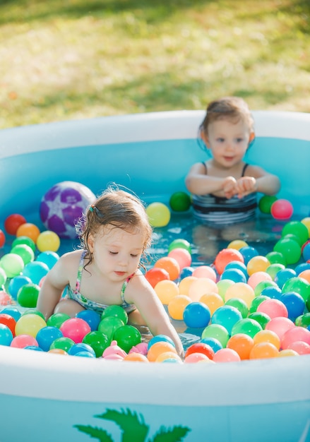 Free photo the two little baby girls playing with toys in inflatable pool in the summer sunny day