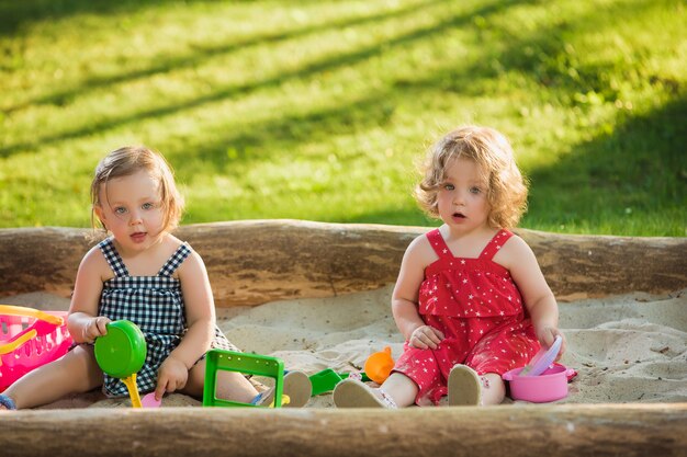 緑の芝生と砂でおもちゃを遊んでいる2人の小さな女の赤ちゃん2歳