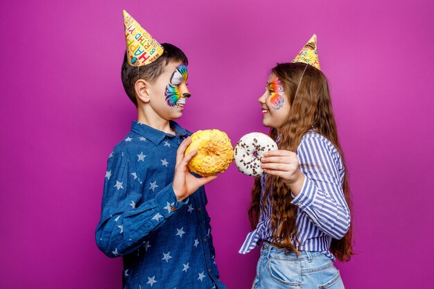 Two little best friends holding sweet and colorful donut isolated on violet wall