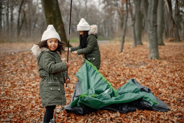 Two little black girls in tent camping in the forest Two little sisters are puting up a tent in autumn forest Black girls wearing khaki coats and beige hats