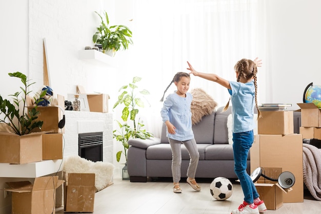 Two little daughters celebrating moving day, excited by relocation into new house, laughing living room with cardboard boxes