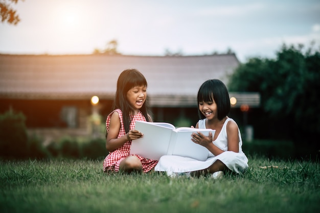 Two little girl friends in the park on the grass reading a book and learn