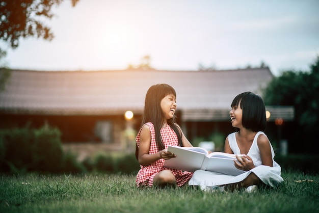 Due piccoli amici della ragazza nel parco sull'erba che legge un libro e impara