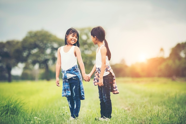 2つの小さな女の子が一緒に公園で楽しいを持って手を
